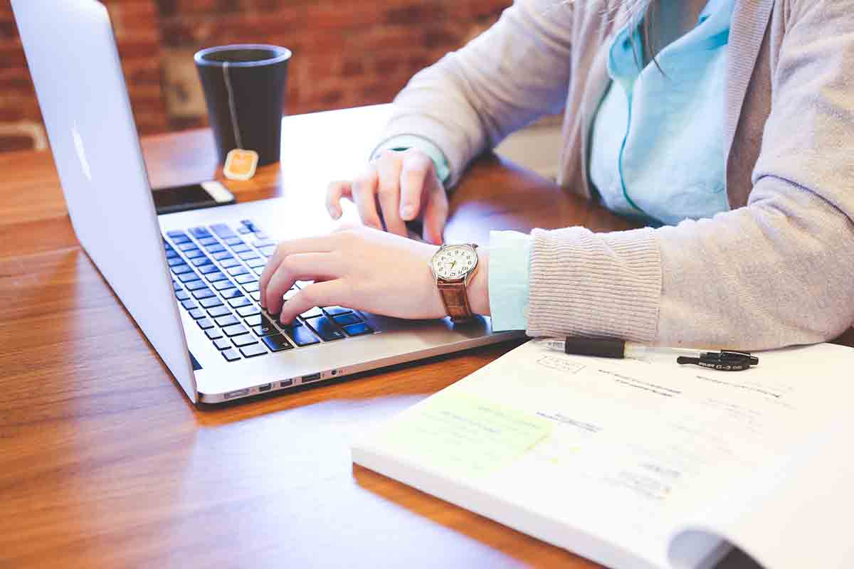 Eine Person arbeitet an einem Laptop. Der Kopf ist ausgeschnitten und der Schreibtisch ist im Fokus.