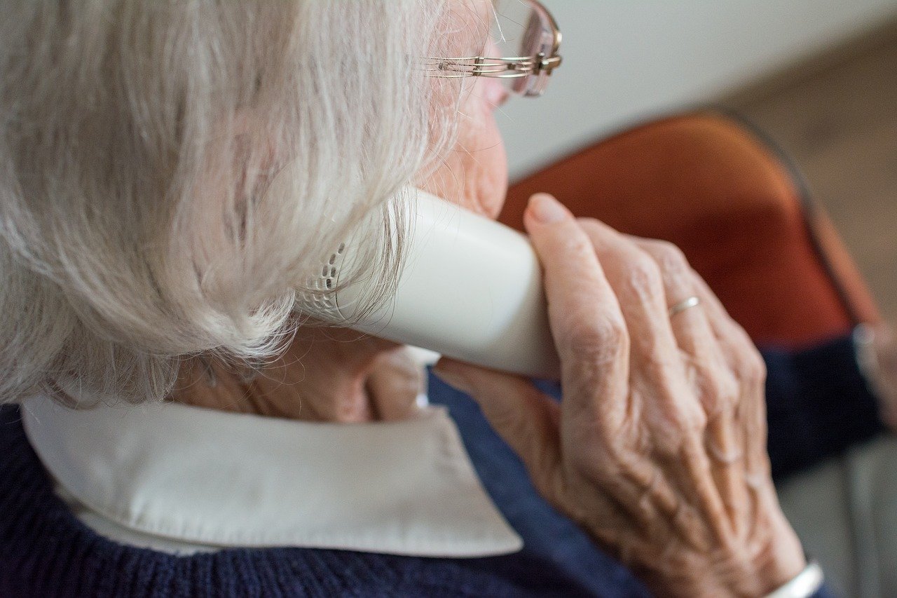 Grauhaarige ältere Dame hält den Hörer eines schnurlosen Telefons