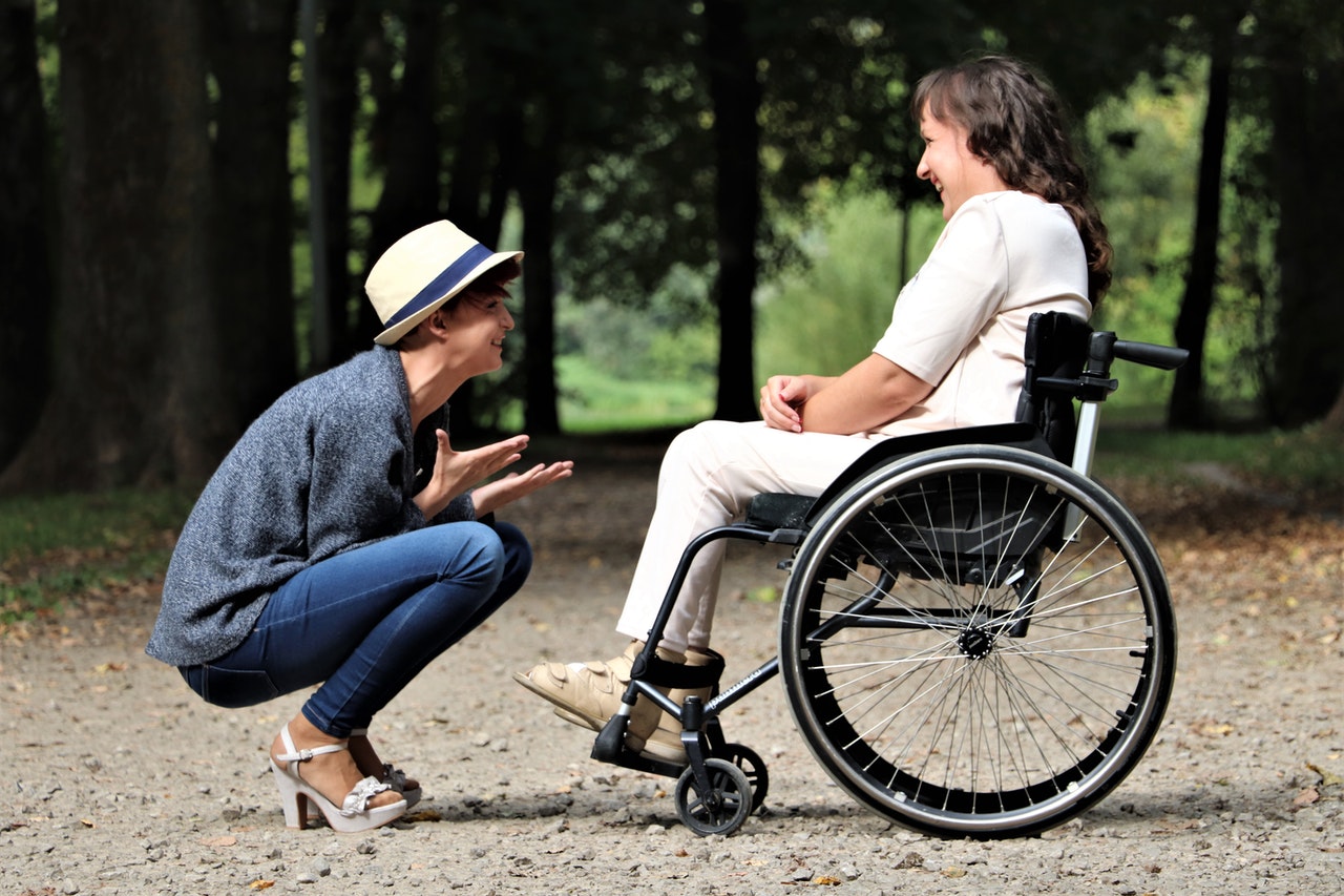 Zwei Frauen unterhalten sich im Park. Eine von ihnen sitzt in einem Rollstuhl.