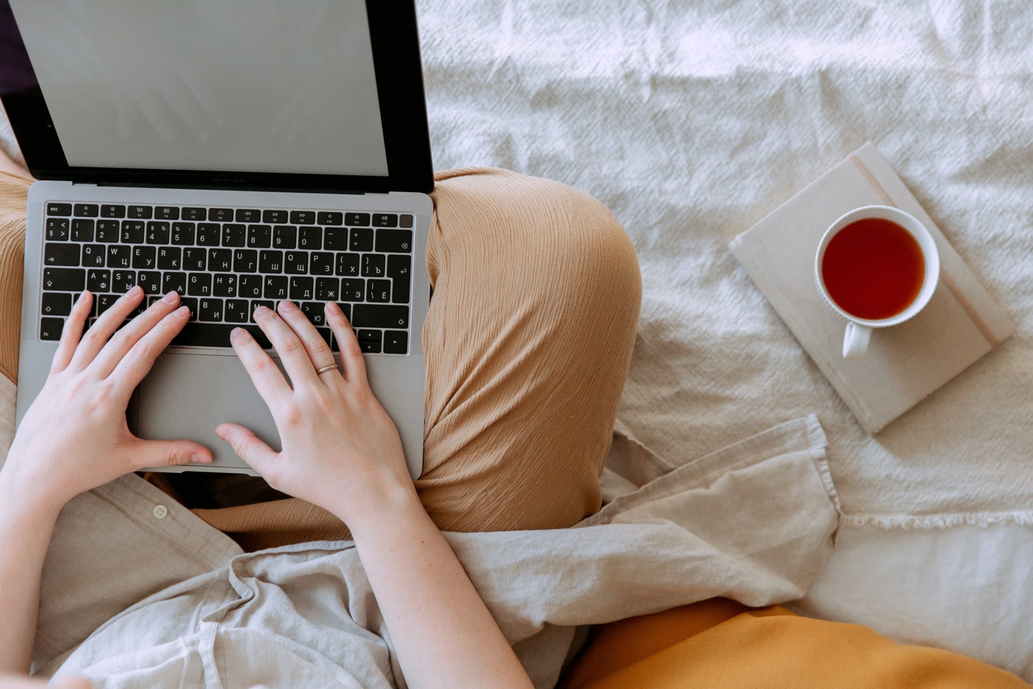 Person sitzt mit Laptop auf dem Schoss auf dem Bett