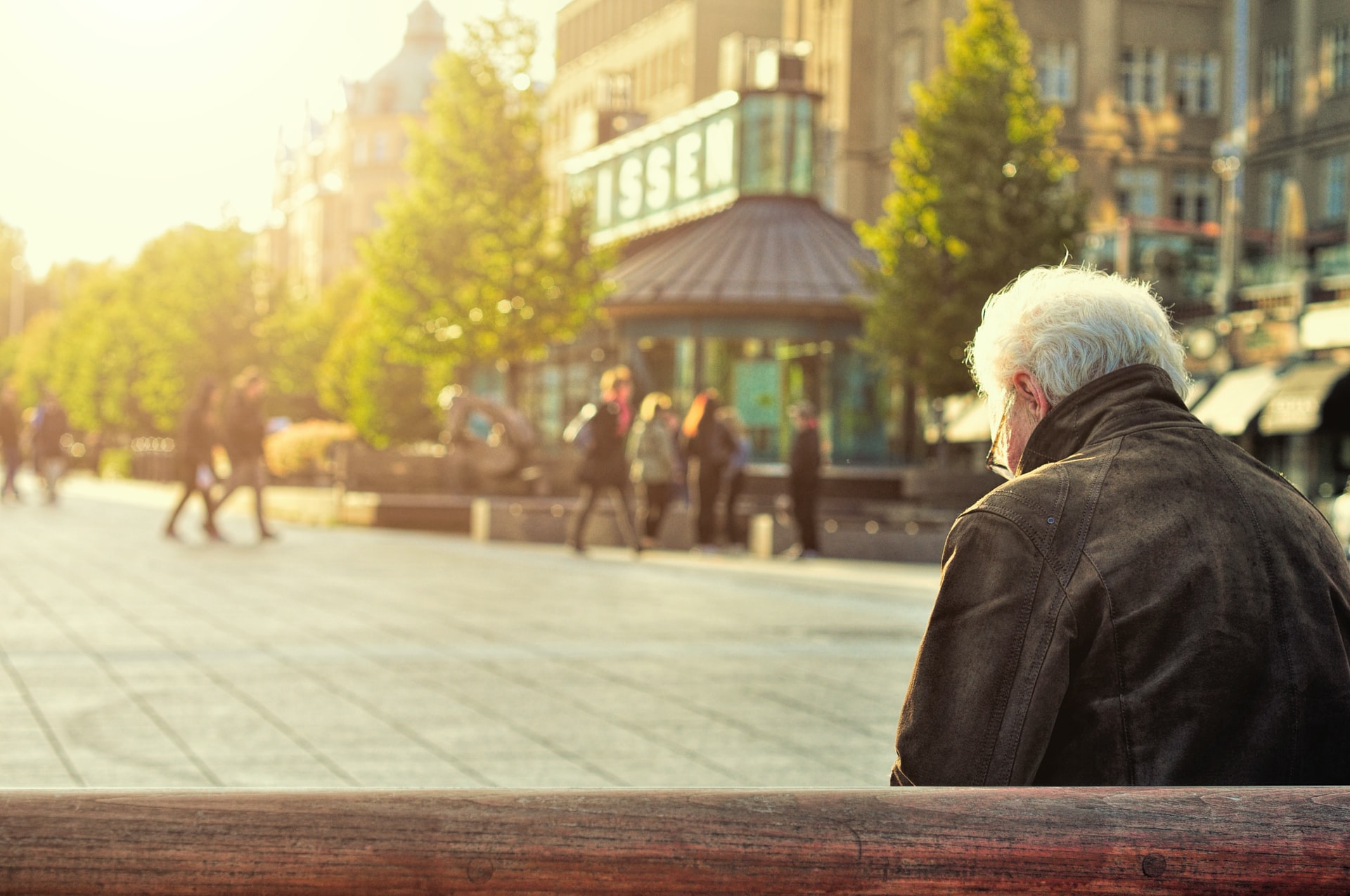 Ein Senior sitzt auf einem Back und betrachtet einen öffentlichen Platz.