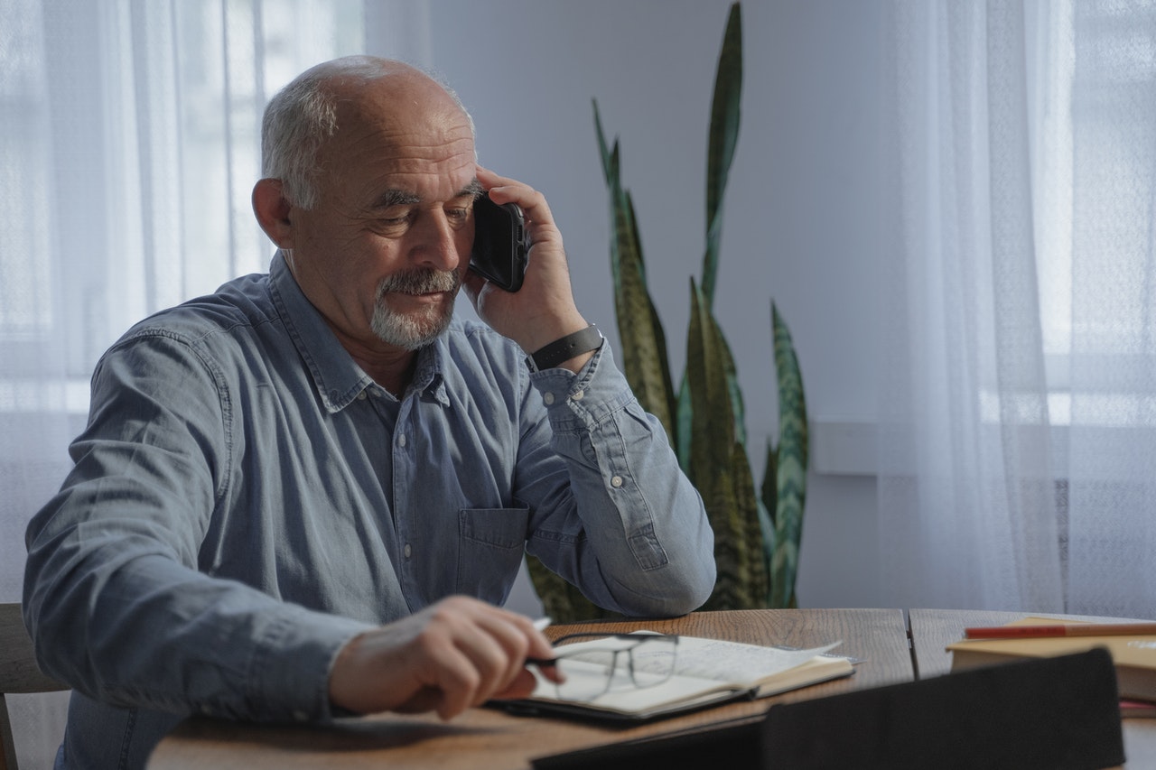 Ein Senior sitzt an einem Tisch und telefoniert.