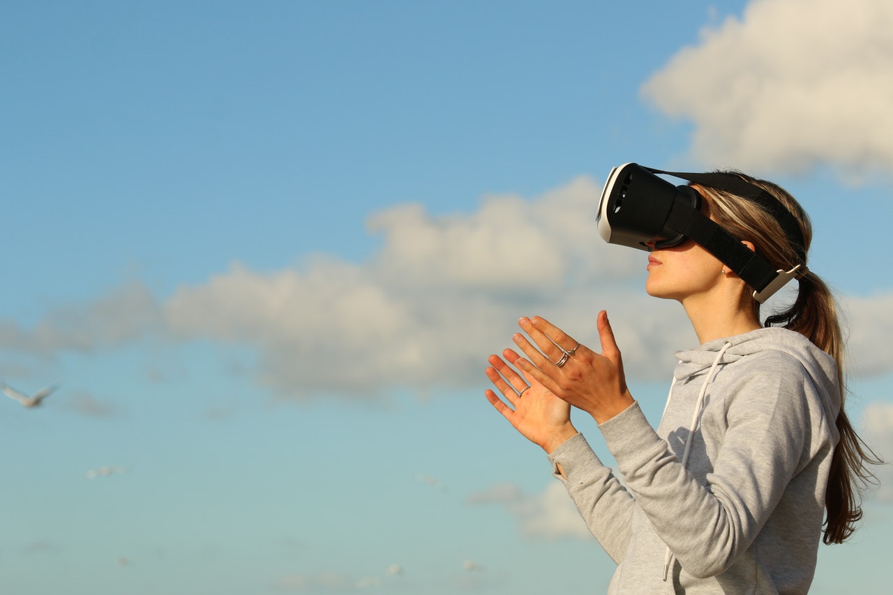 Eine Frau steht mit einer VR-Brille unter freiem Himmel und macht eine fragende Geste.