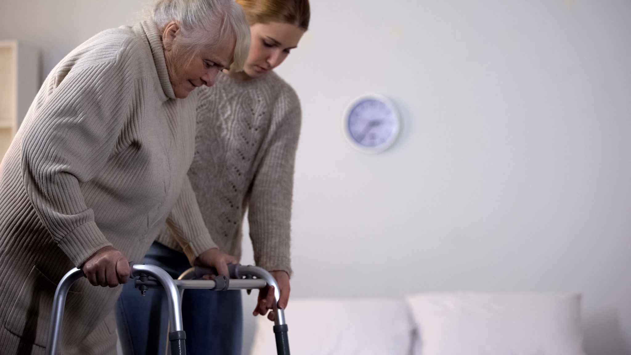 Eine junge Frau hilft einer Senioren am Rollator zu gehen.