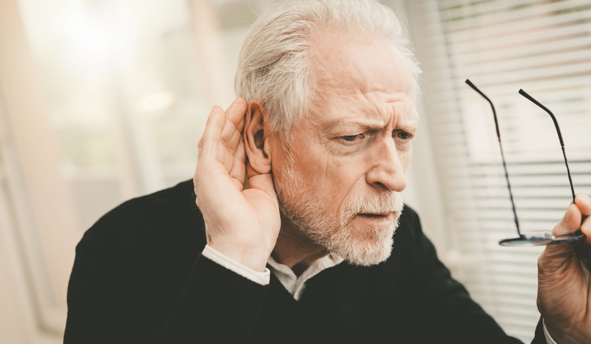 Ein Senior hört slecht und hält sich deshalb eine Hand ans Ohr.