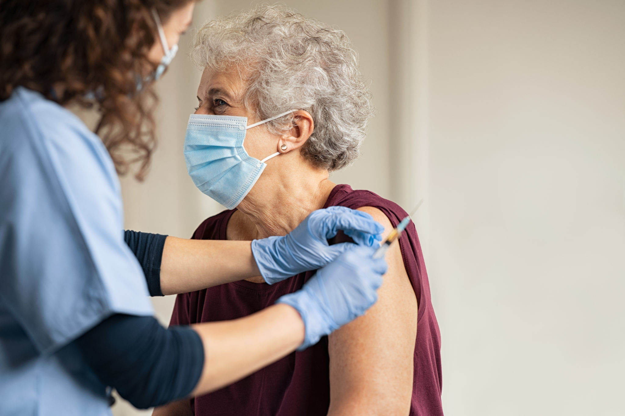 Eine Seniorin erhät eine Schutzimpfung. Alle tragen eine medizinische Maske.