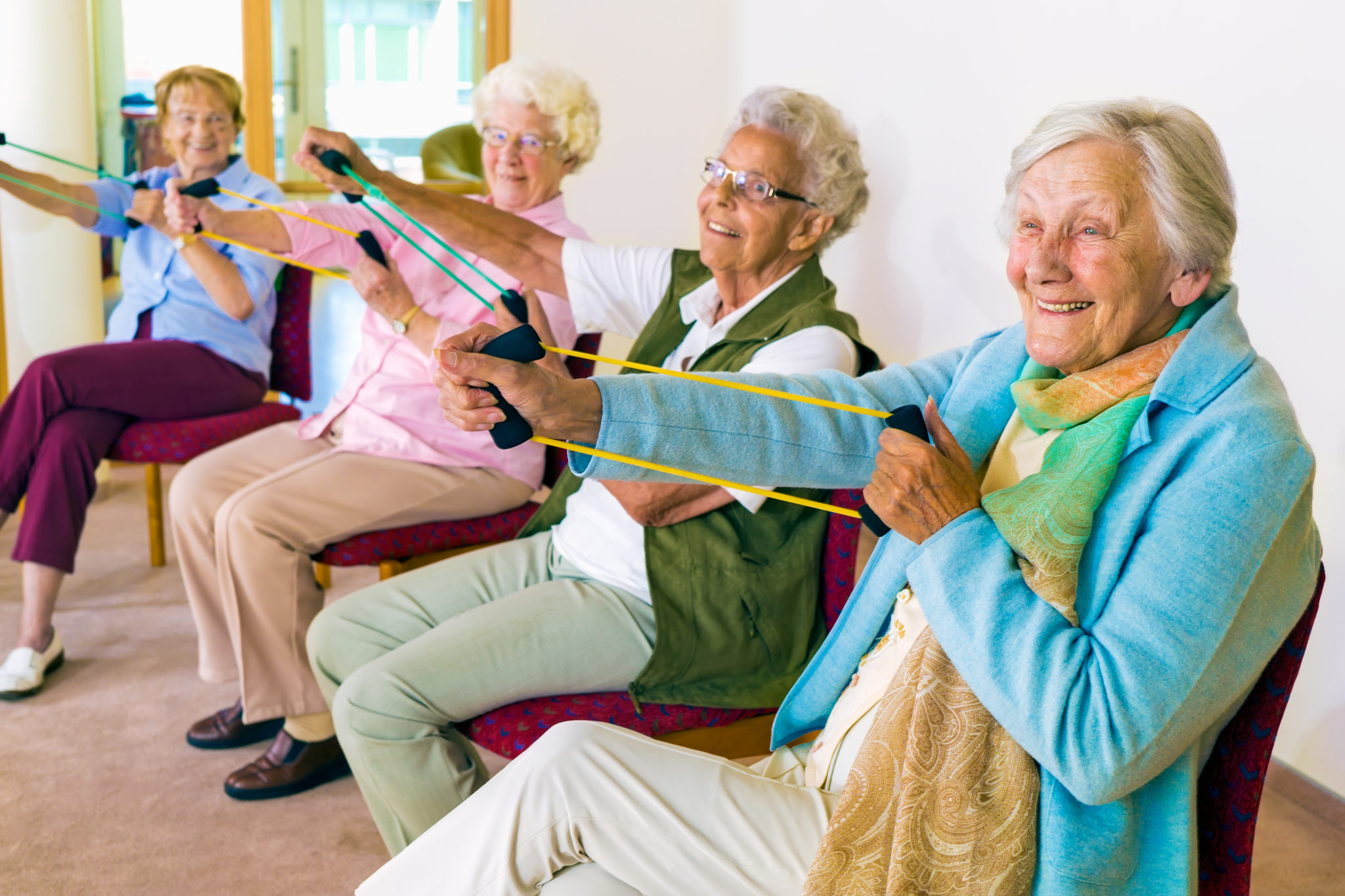 Vier Seniorinnen machen gemeinsam Sport und nutzen ein Tube als Trainingsgerät.