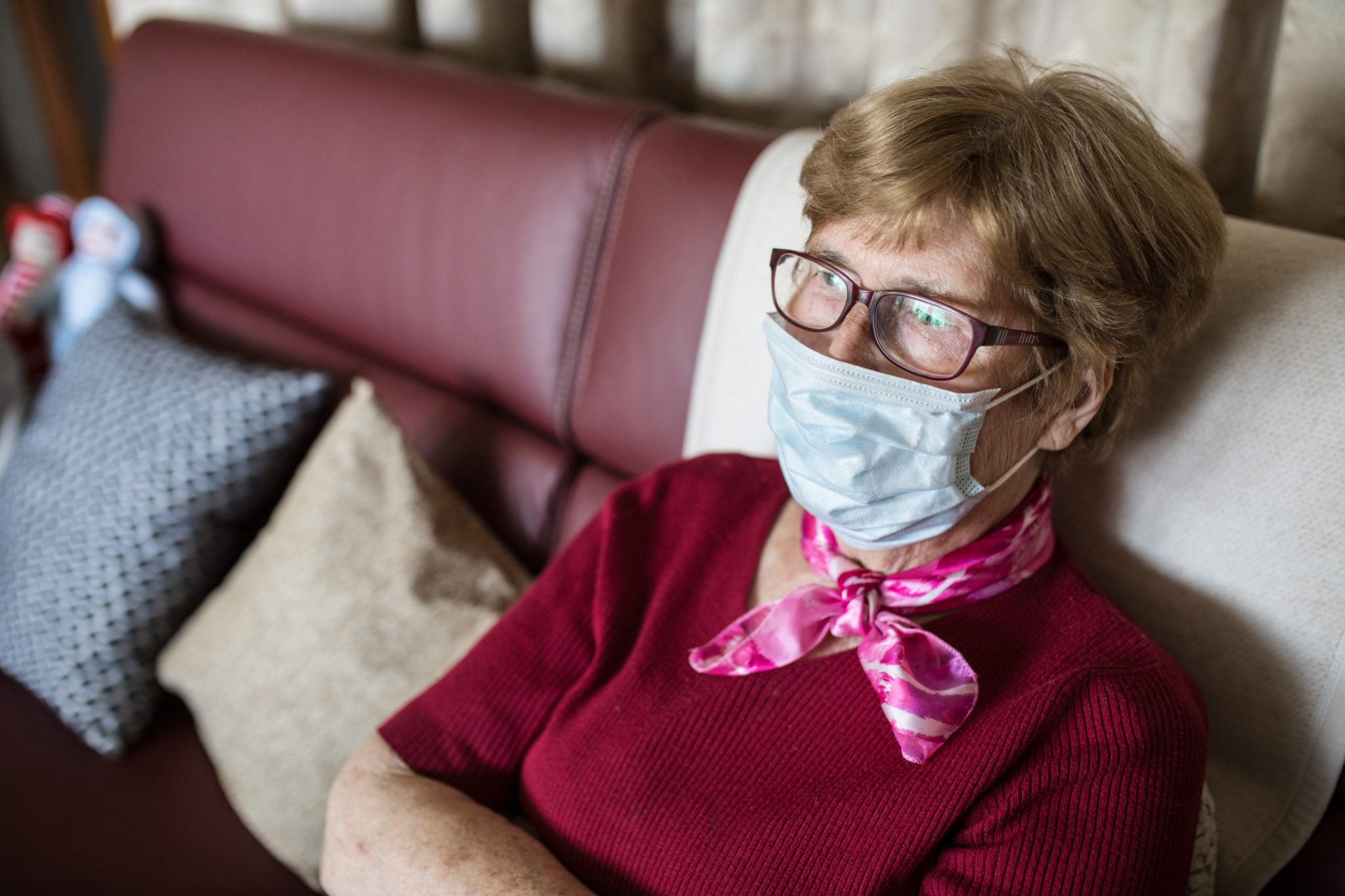 Eine Seniorin sitzt mit Maske auf ihrem Sofa.