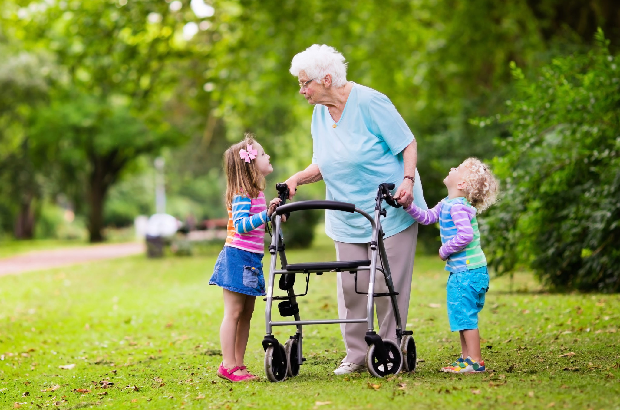 Eine Senioren spielt mit zwei Kindern im Garten, während sie an einem Rollator geht.