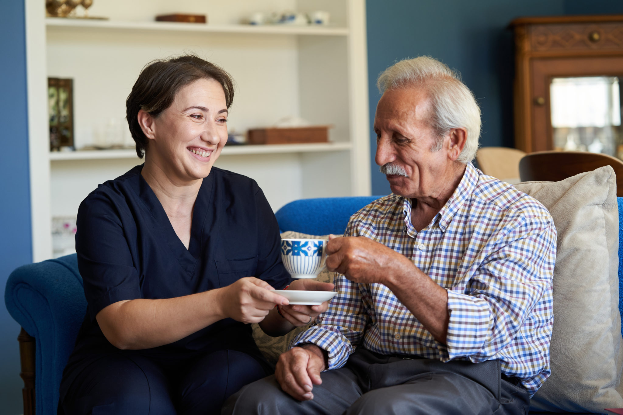 Eine Frau reicht ihrem pflegebedürftigen Vater eine Tasse Kaffee.