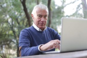Älterer Mann sitzt im Garten an einem Laptop