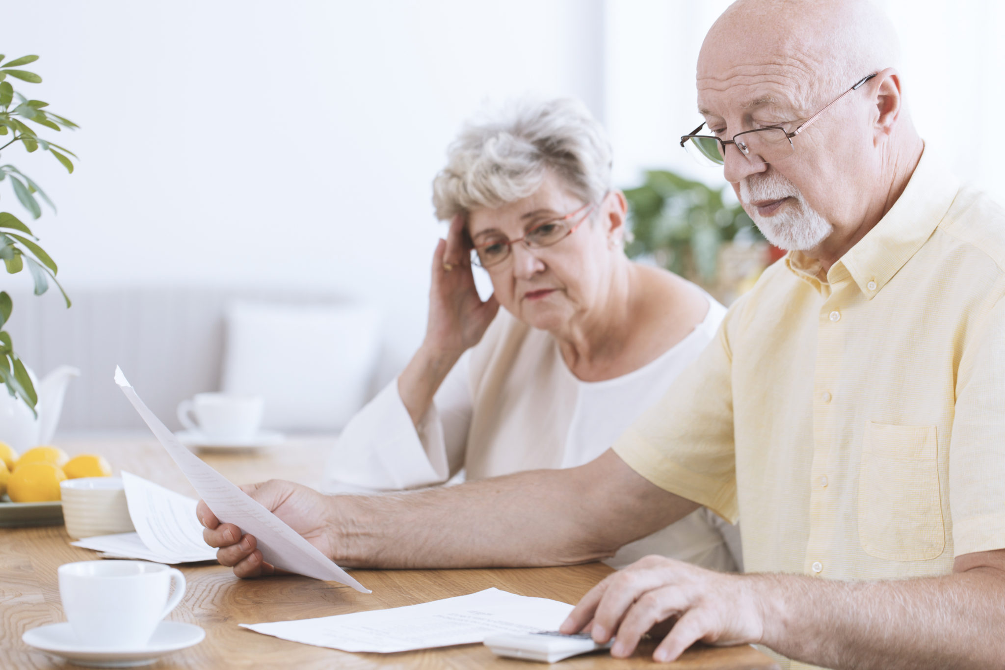 Ein Seniorin und ein Senior betrachten ein Blatt Papier und bedienen parallel einen Taschenrechner.