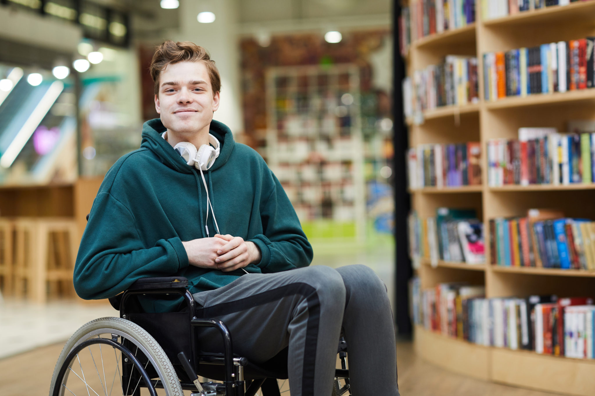 Ein junger Mann besucht im Rollstuhl eine Bibliothek.