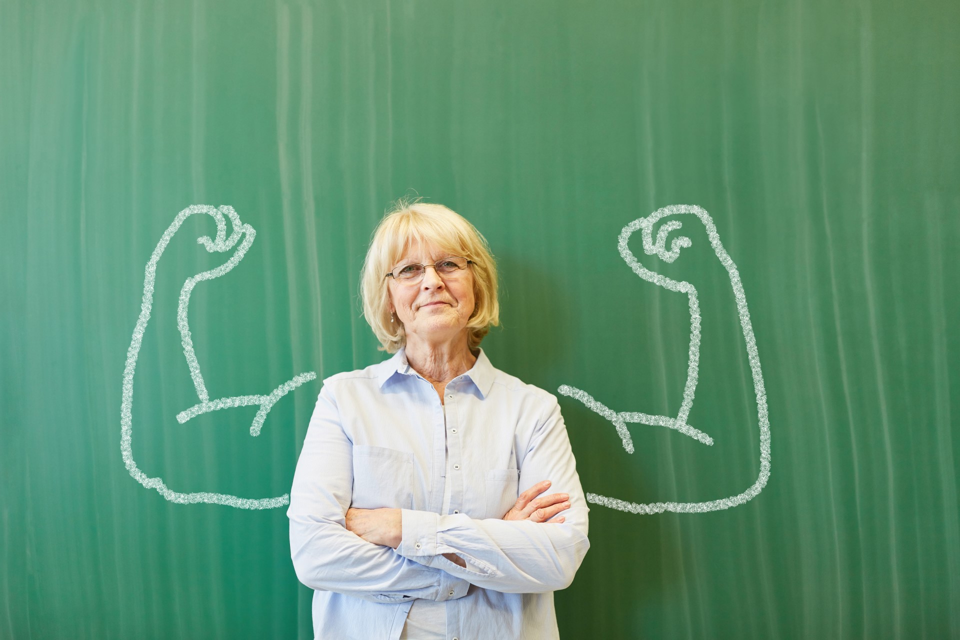 Eine Frau steht vor einer Tafel. Rechts und links von ihr wurde ein starker Arm auf die Tafel gemalt. Dies steht für Resilienz.