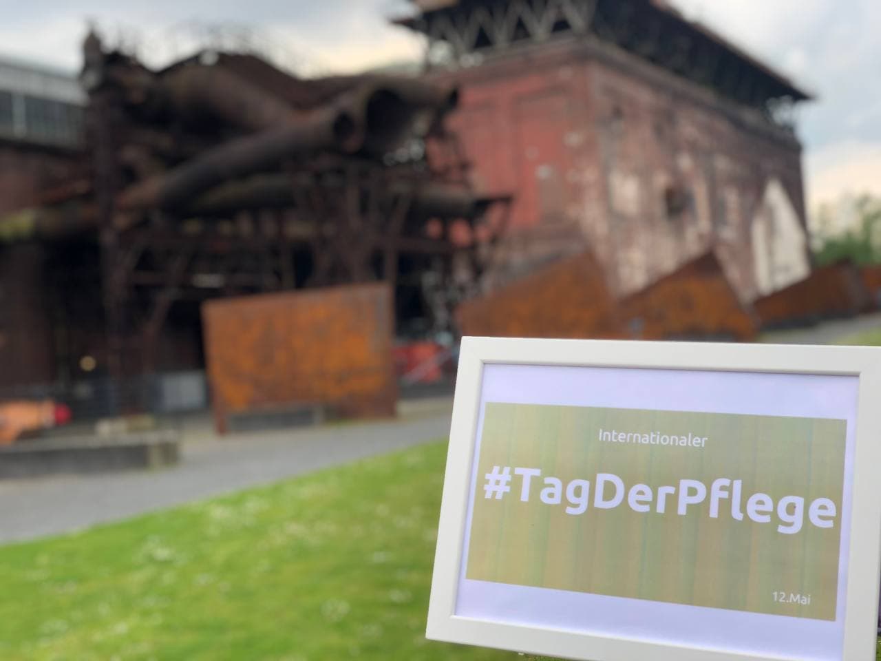 Foto der Jahrhunderthalle Bochum, im Vordergrund ein Bilderrahmen mit dem Text "Internationaler Tag der Pflege"