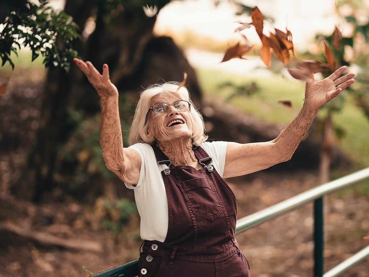 Eine Seniorin wirft glücklich Blätter in die Luft.