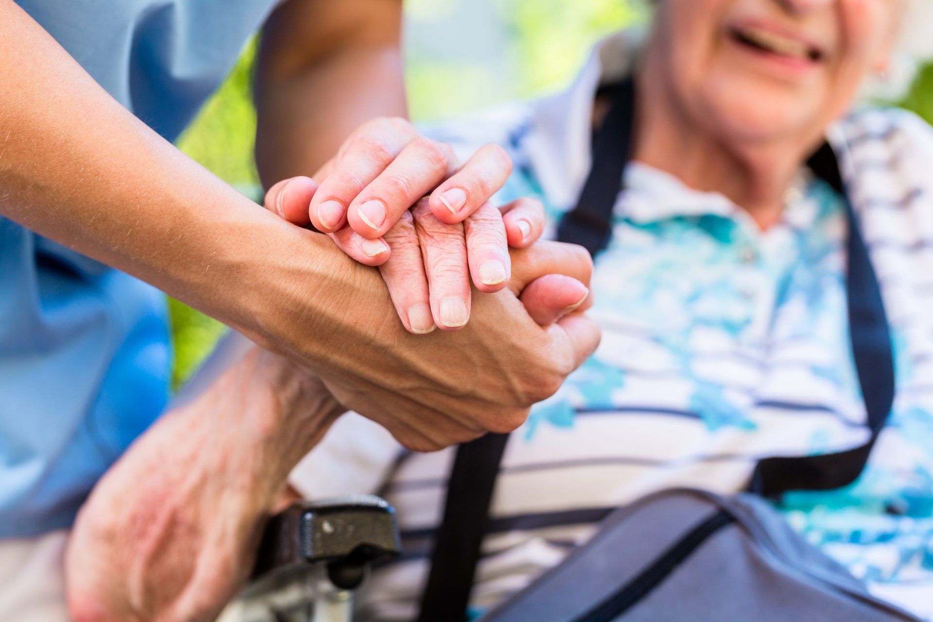 Ein junger Pfleger hält die Hand einer Seniorin. Die Seniorin lacht.