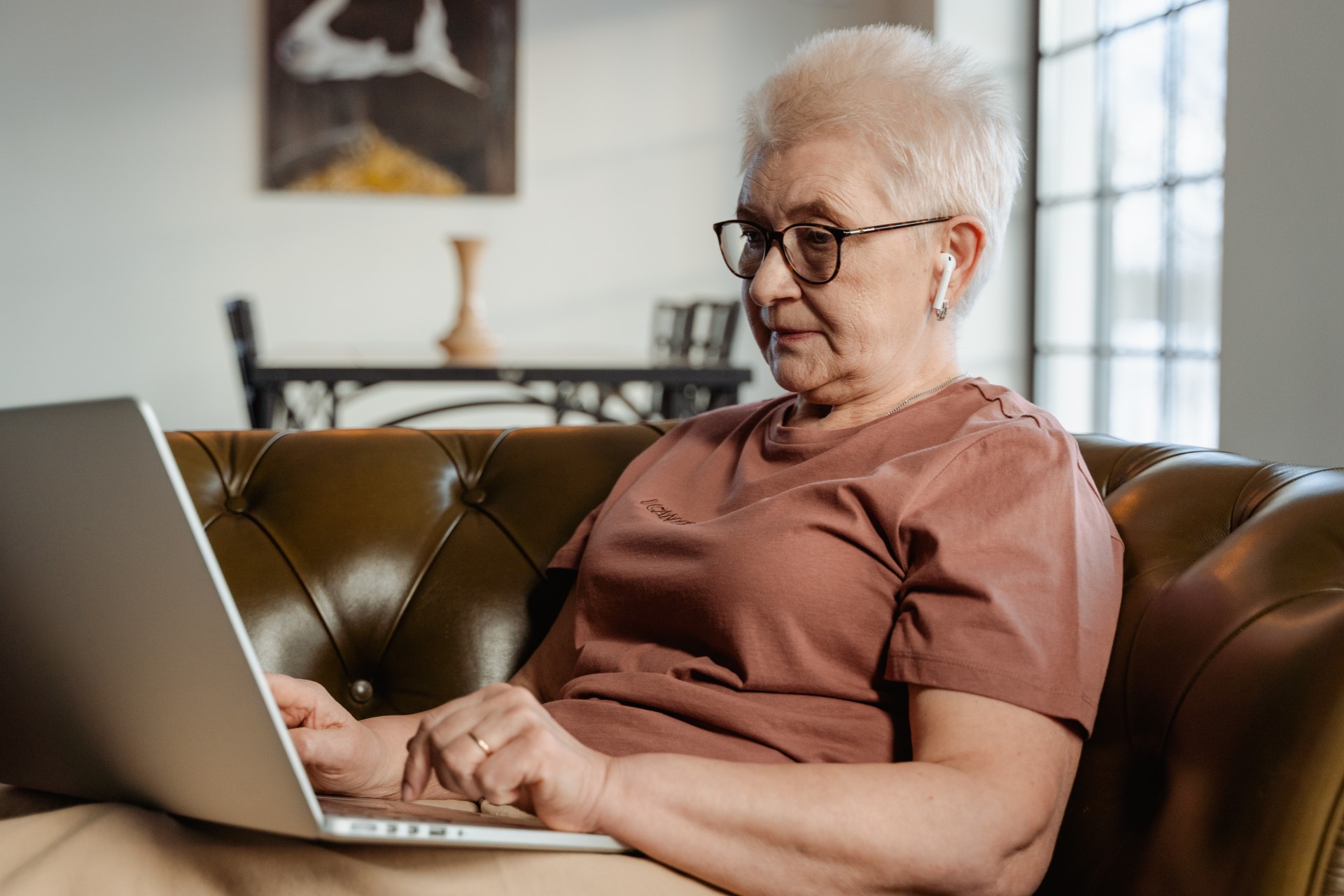 Eine Seniorin sitzt auf der Couch und nimmt über ihren Laptop an einem Online-Seminar teil.