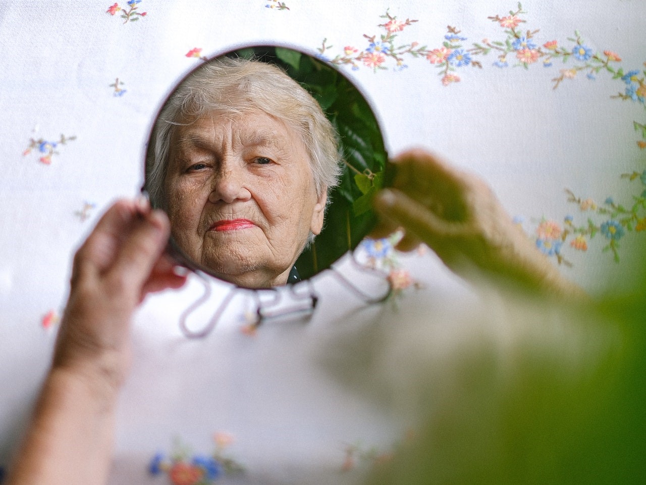 Eine Seniorin betrachtet ihr eigenes Spiegelbild in einem kleinen, runden Spiegel.