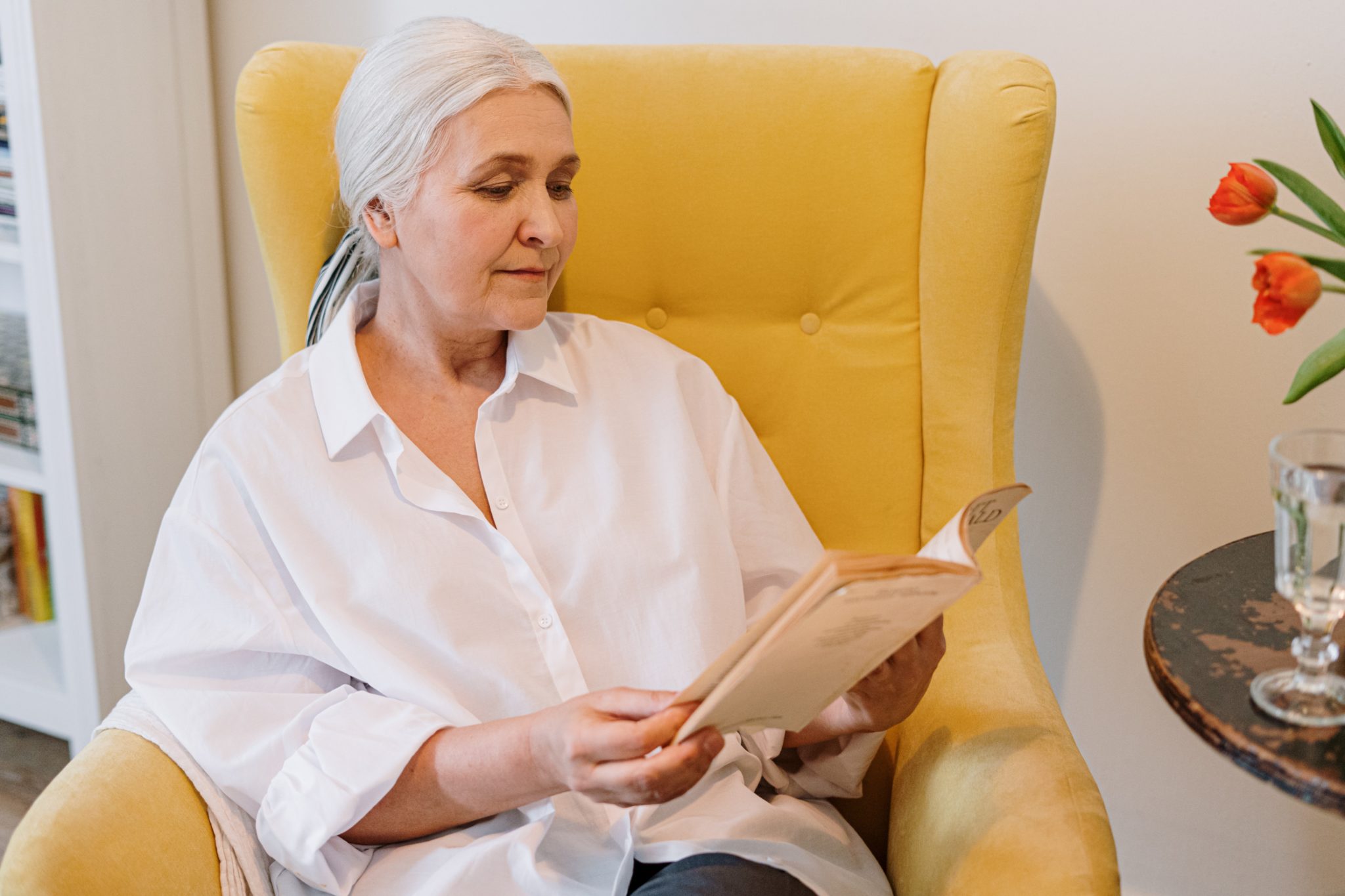 Ältere Dame sitzt in gelbem Sessel und liest ein Buch