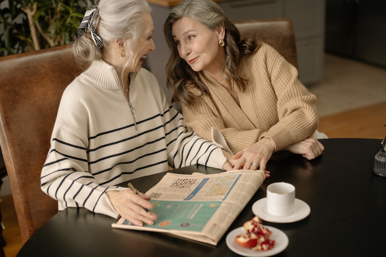 Zwei Seniorinnen sitzen am Kaffeetisch und lachen.