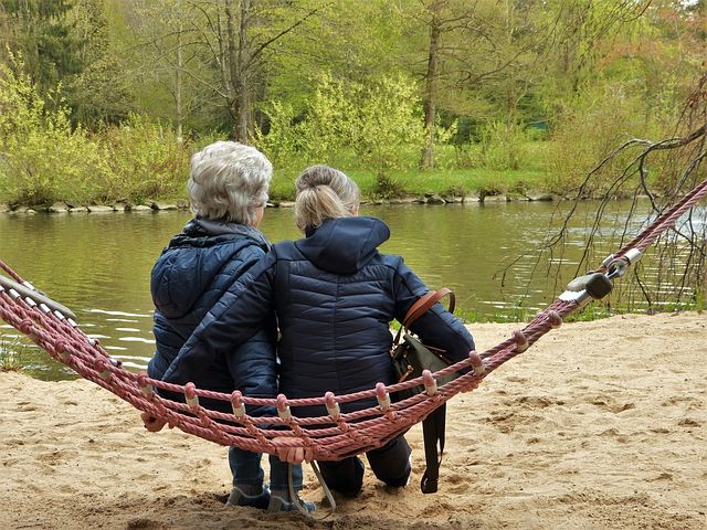 Eine ältere Dame sitzt mit ihrer Begleitung auf einer Hängematte und schaut auf einen See