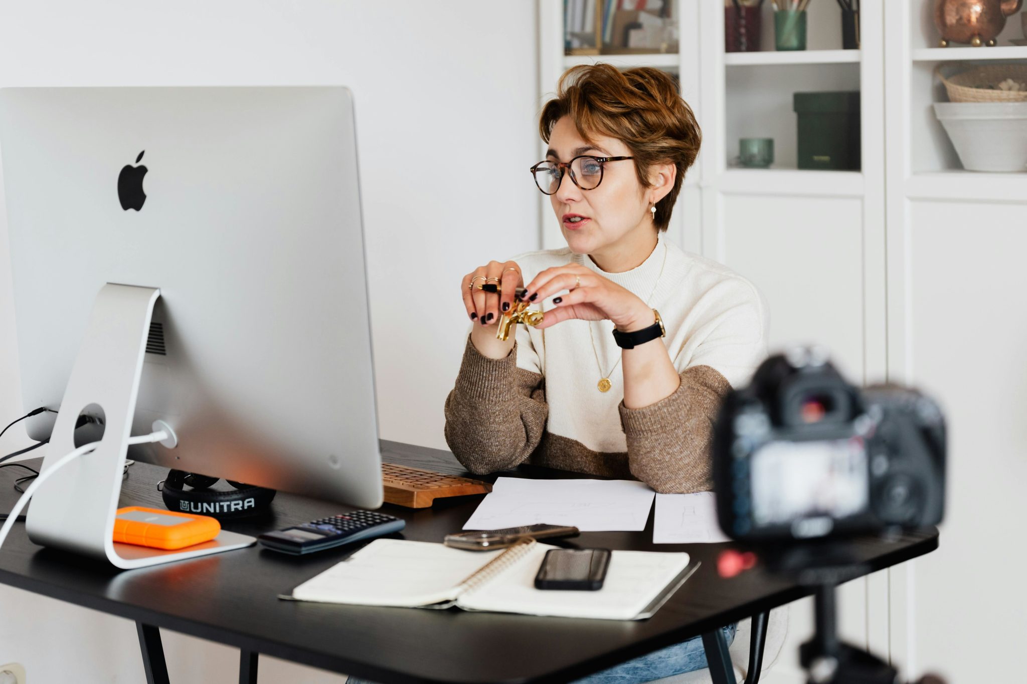 Frau mit Unterlagen und Brille sitzt vor Laptop