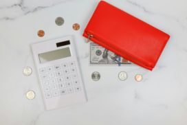 Auf einem Tisch liegt ein Taschenrechner, ein rotes Portemonnaie und loses Geld.