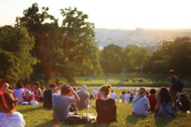 Menschen sitzen im Sonnenuntergang auf einer Wiese beieinander.