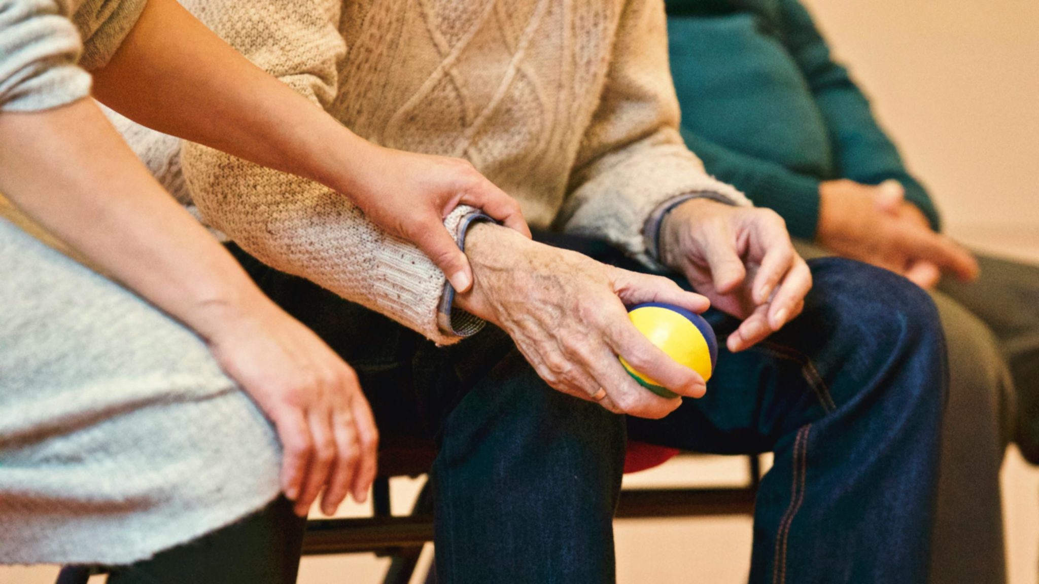 Man sieht die Hand eines älteren Mannes mit einem Ball. Darüber liegt die Hand einer anderen Person