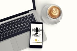 Man sieht ein Handy, auf dem ein Podcast läuft auf einem Laptop, daneben eine Tasse Kaffee
