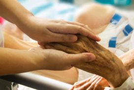 Man sieht zwei jüngere Hände, die eine ältere Hand in ihren Händen hält
