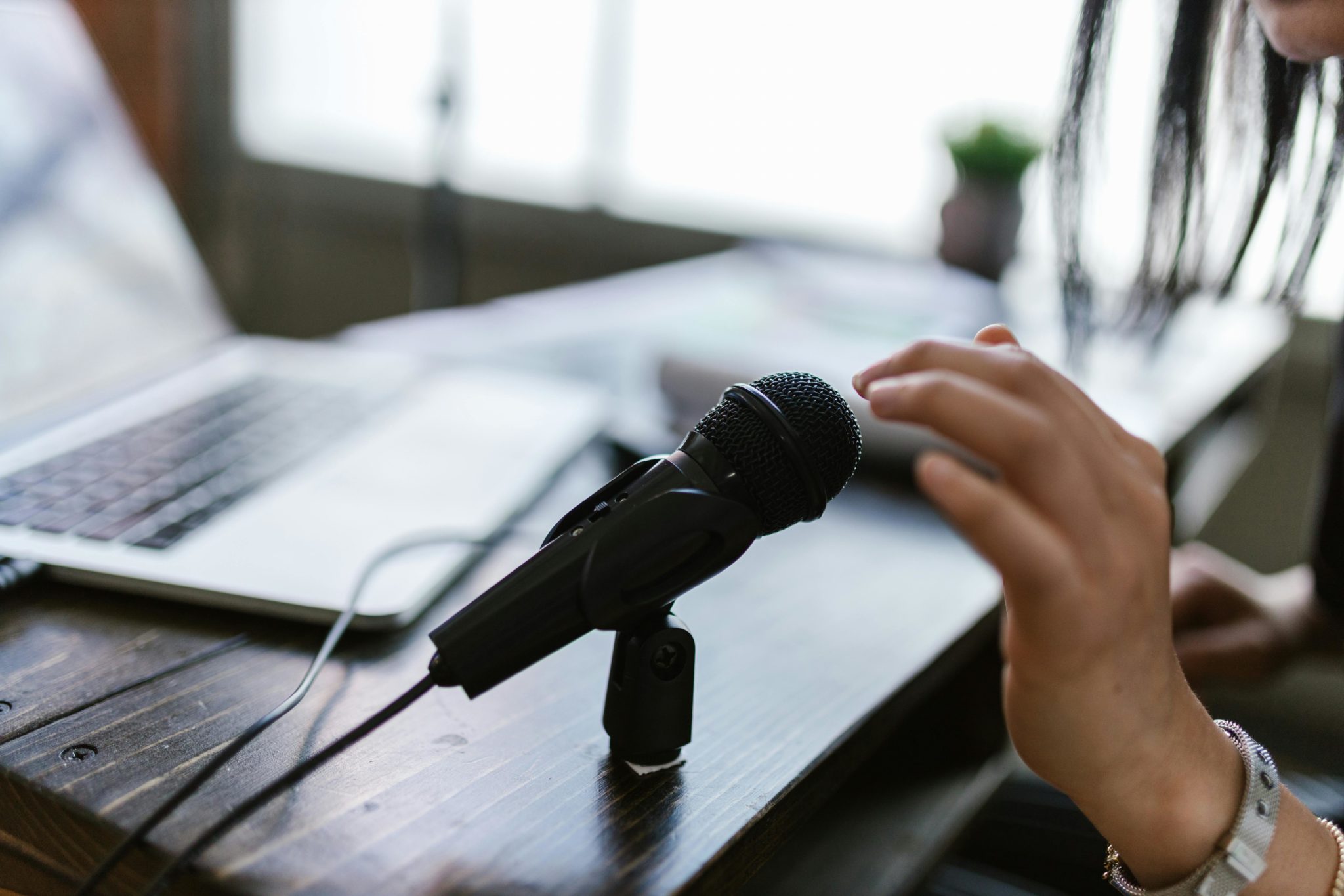 man sieht eine Hand über einem Mikrofon, das Foto suggeriert die Aufnahme eines Podcasts