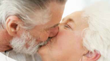 Das Bild zeigt ein sich küssendes Paar (Mann und Frau). Beide haben graue Haare.