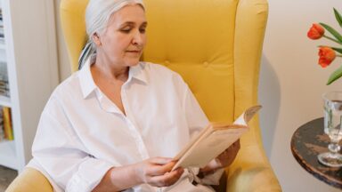 Eine Seniorin sitzt in einem Sessel uns liest in einer Zeitschrift.
