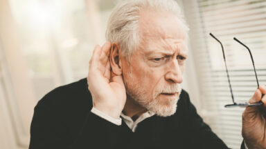 Ein Senior hört slecht und hält sich deshalb eine Hand ans Ohr.