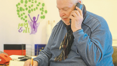 Ein Mitarbeiter des Kontaktbüros Pflegeselbsthilfe Herford hilft über das Telefon dabei einen Impftermin zu vereinbaren.