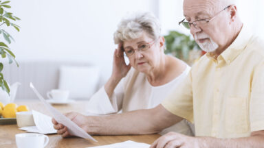 Ein Seniorin und ein Senior betrachten ein Blatt Papier und bedienen parallel einen Taschenrechner.