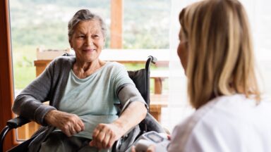 Einer Seniorin in einem sitzen in einem Rollstuhl in lächelt ihr Gegenüber an.