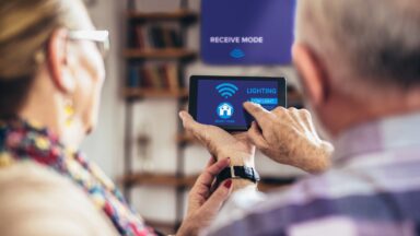 Eine Seniorin und ein Senior entdecken smart home. Sie schalten das Licht mit einem Handy an.
