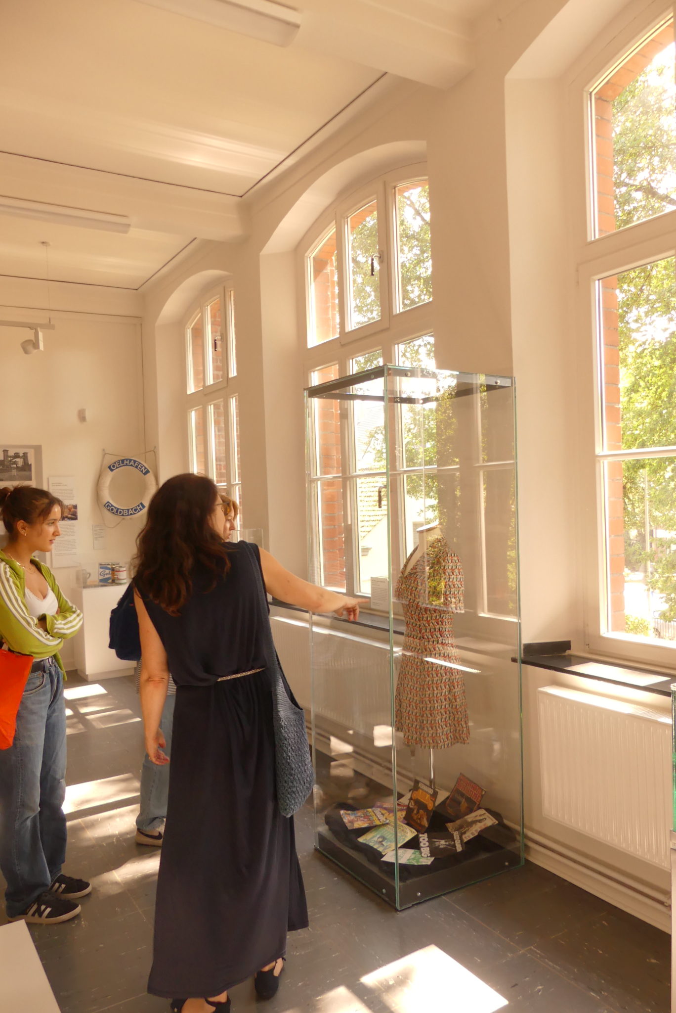 Teilnehmende besichtigen eine Vitrine, in der ein Kleid der 60er Jahre ausgestellt ist