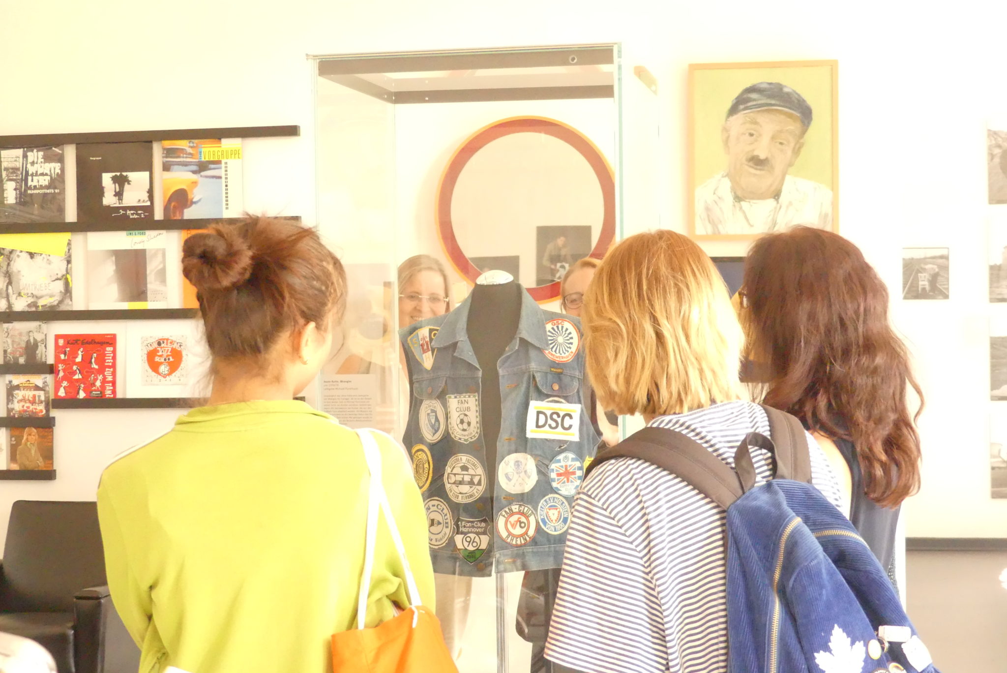 Teilnehmer*innen stehen um eine Vitrine, in der eine Jeansweste mit Fußballemblemen ausgestellt ist