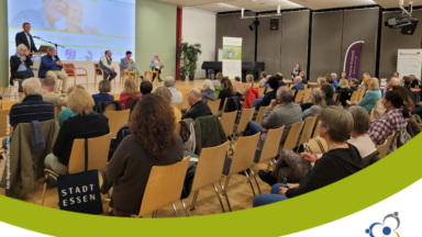 Veranstaltung mit Menschen auf einer Bühne und Publikum davor sitzend