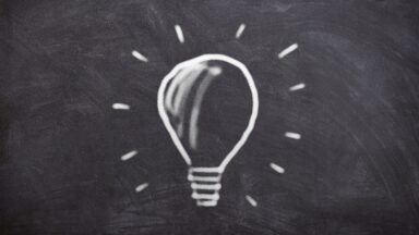 Weiß gerandete Zeichnung einer leuchtenden Glühbirne auf schwarzem Hintergrund