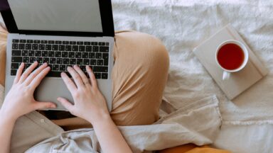 Person sitzt mit Laptop auf dem Schoss auf dem Bett