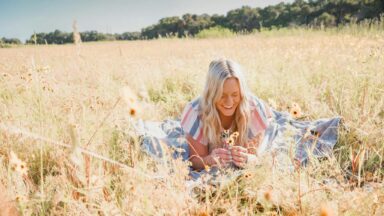 Blone Frau liegt entspannt im sommerlichen Kornfeld.