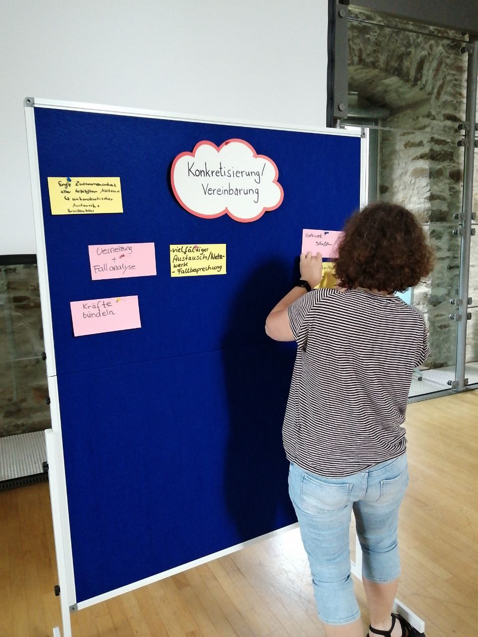 Eine Teilnehmerin heftet eine karte an die metaplanwand zum Thema "Konkretisierung und Vereinbarung"