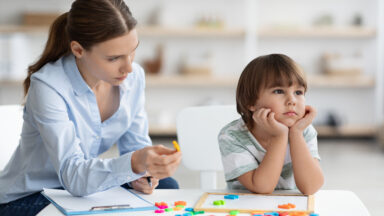 Bored sad little boy refusing to cooperate with his private teacher, ignoring speech therapist with colorful letters at office, free space